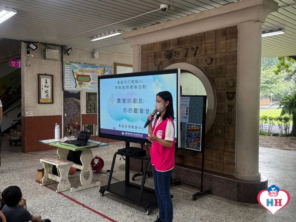 社工穿著粉紅色背心,站在螢幕前向學生宣導聽力與輔具相關知識。